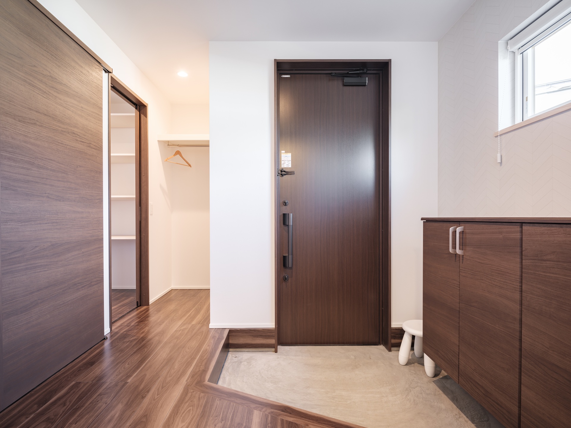 玄関ドアの横に扉のないシューズクロークを配置し、反対側に低い靴箱を設けて圧迫感を抑えた、機能的でスッキリとした玄関の間取り事例