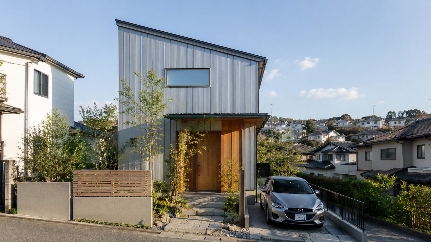 横浜市金沢区の穏やかな坂道に建つ、シンプルモダンな外観の戸建て住宅。1台分のカースペースと外構植栽のある風景