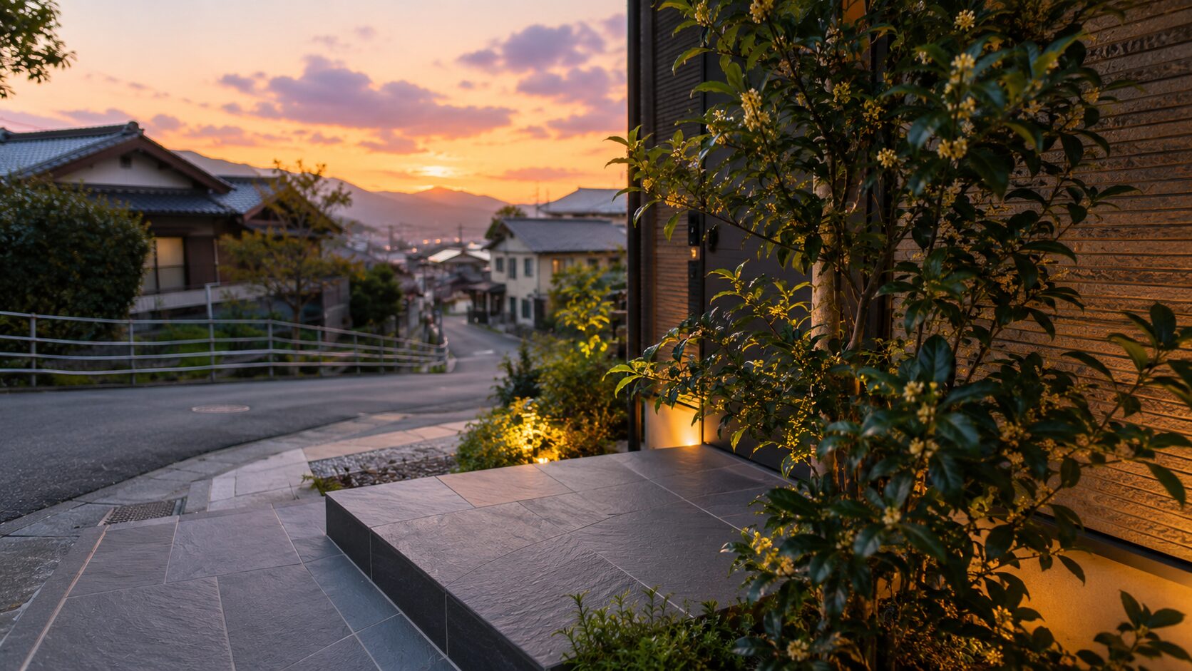 夕焼け空が広がる閑静な住宅街の坂道と、植栽が美しく整えられた玄関アプローチ